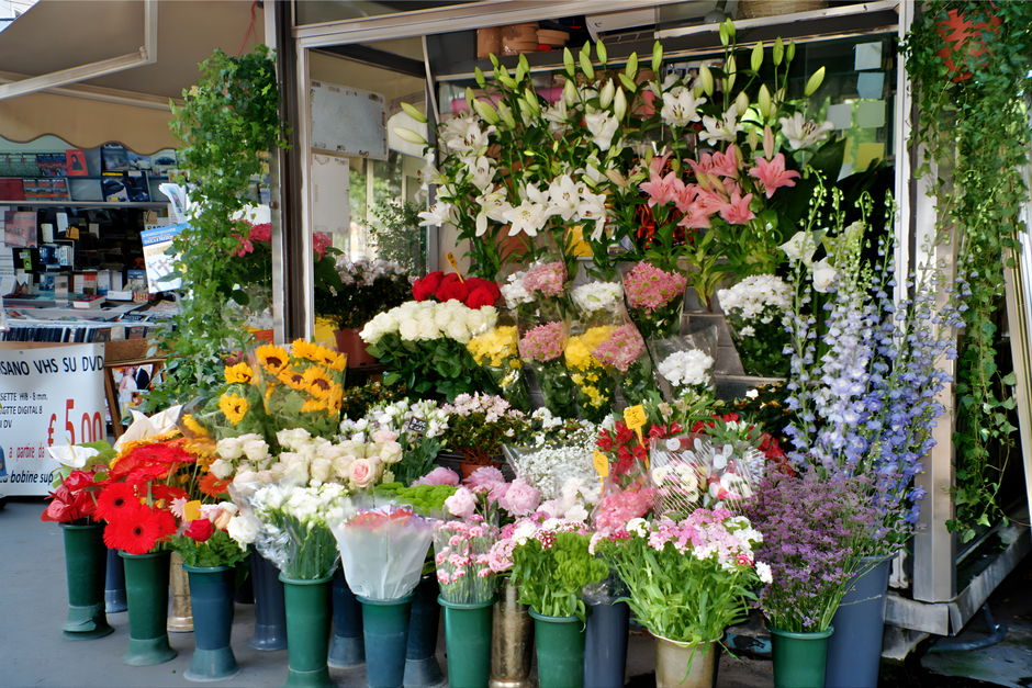 A vibrant display of fresh floral arrangements outside a flower shop, featuring a variety of flowers in different colors and styles. Tall pink and white lilies with partially opened buds sit prominent