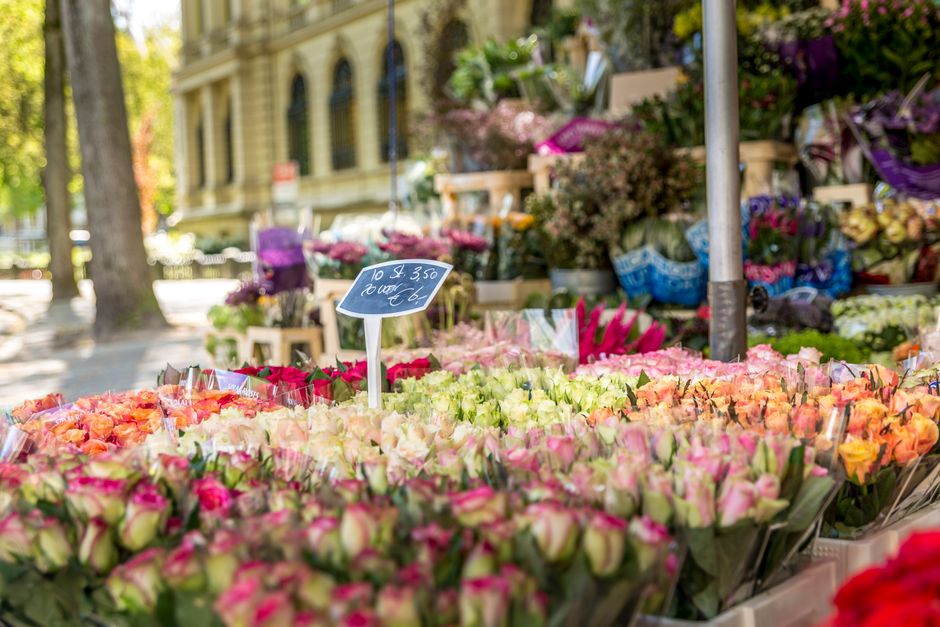 A vibrant outdoor flower market stand featuring an extensive display of fresh flower bouquets arranged in neat rows, predominantly showcasing pink, peach, and cream-colored roses with delicate petals 